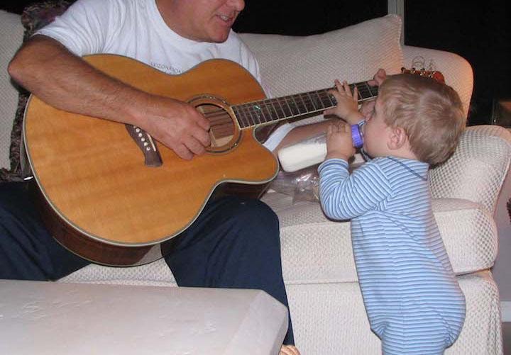 Father playing guitar while toddler reaches for the strings — an early love of music