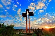 Tall wooden cross standing against a dramatic blue sky with clouds at sunset